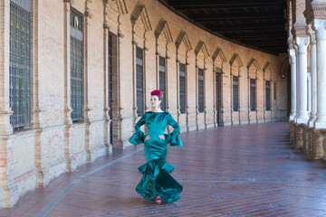 Young and beautiful woman with typical green dress with ruffles and dancing flamenco in plaza de...