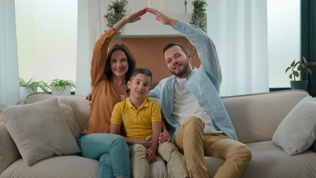 Happy smiling Caucasian family homeowners mother father son parents kid boy child sitting on couch in cozy living room make roof with hands dwelling symbol looking at camera new rented house bank loan