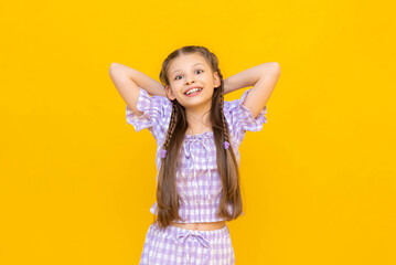 A beautiful little girl is smiling happily. A young girl posing in a summer suit. A happy, joyful child on a yellow isolated background.