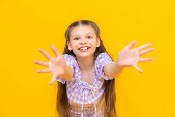 A beautiful little girl stretches her arms out, palms forward, and smiles broadly. A happy child. Yellow isolated background.