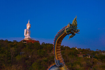 Large Naga Statue and large white Buddha statue with blue sky at Wat Roi Phra Putthabat Phu...
