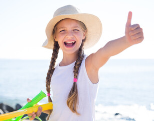 Child in hat on beach shows thumb up