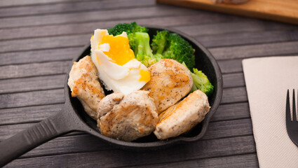 Healthy appetizer of chicken pieces with broccoli and poached egg in small cast iron skillet