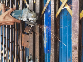Man cuts the lock or padlock on old steel metal shutter and folding door gate with an angle...