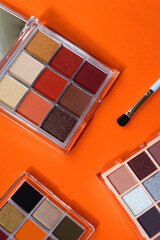 Colorful eyeshadow palettes and make up brush on orange background. Top view.