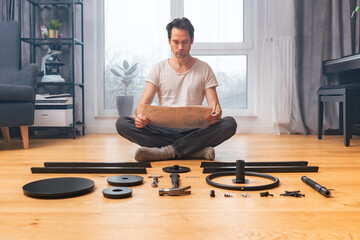 A man is carefully studying the instructions for self-assembly of furniture, sitting cross-legged...