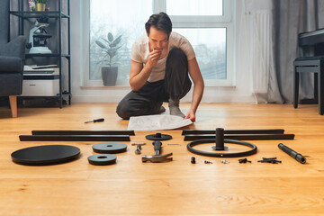 A man sitting on the floor in a room among carefully laid out parts and tools is carefully studying...