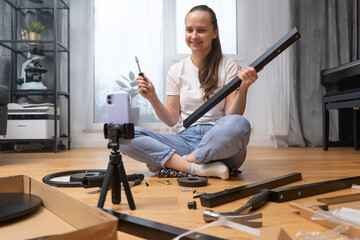 A vlogger girl records a video tutorial on assembling furniture for her channel on her phone...