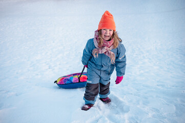 Portrait of a child playing in the snow in winter, sliding down the hill on a tubing