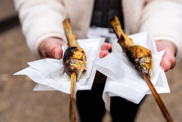 Obraz premium Ayu fish grilled with salt, in woman hand. Japanese ayu sweetfish a famous Japan street food.