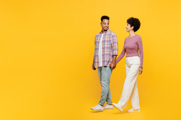 Full body side view young couple two friend family man woman of African American ethnicity wear purple casual clothes together hold hand walk go stroll look camera isolated on plain yellow background - Powered by Adobe