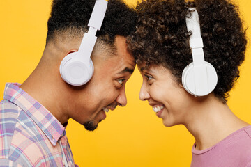 Young couple two friend family man woman of African American ethnicity wear casual clothes together listen to music in headphones look to each other touch forehead isolated on plain yellow background - obrazy, fototapety, plakaty
