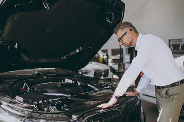 Side view adult man customer male buyer client wears shirt examining engine open car hood choose...