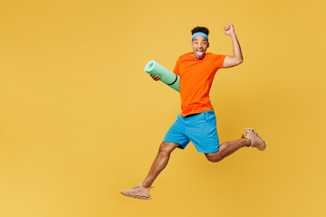 Fototapeta na wymiar Full body side view young fitness trainer sporty man sportsman wear orange t-shirt jump high with yoga mat run training in home gym isolated on plain yellow background. Workout sport fit abs concept.