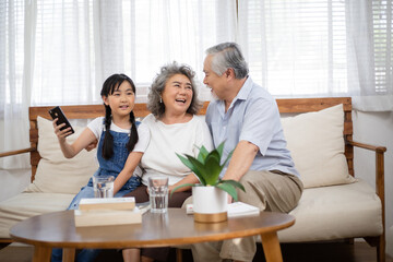 Asian senior couple enjoy talking with granddaughter in the living room. Little girl visit her grandparents at home on holidays weekend. Love and bonding family spending time together.