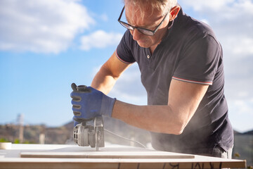 Caucasian worker with gloves holding an angle grinder for cutting metal, stone and ceramic.