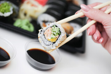 Sushi background. Woman hand holding chopsticks. Uramaki salmon roll. Japanese food isolated on white table. Eating sushi with dark soy sauce. Takeaway sushi lunchbox. Dipping sushi in soy sauce.
