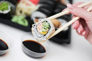 Foto op Plexiglas Sushi background. Woman hand holding chopsticks. Uramaki salmon roll. Japanese food isolated on white table. Eating sushi with dark soy sauce. Takeaway sushi lunchbox. Dipping sushi in soy sauce. © Paweł Michałowski