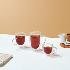a variety size of transparent double wall glass with tea inside it, on a white and beige colored background.