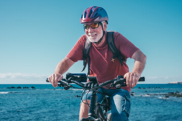 Portrait of active senior man with helmet enjoying riding bike at sea to be fit and healthy....