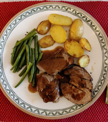 Dinner: Lamb in gravy with baked potato halves and green beans on dinner plate with pretty décor on a red placemat