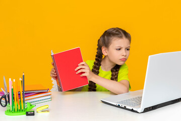 A little girl is doing her homework at a desk with a laptop. Home online education for...