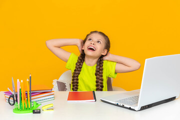 Children's education. A little girl looks up sitting at her desk and wide. Online home education...