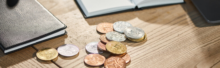 golden and silver bitcoins near notebooks on work desk in contemporary office, horizontal banner
