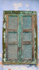vertical image of a window closed with plywood shutters in a wooden frame with peeling paint, as a background exterior detail of an old residential building
