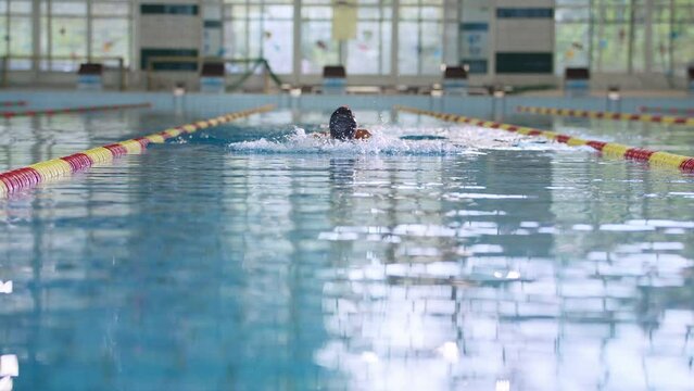 Sportswoman, a professional swimmer using breaststroke drills during a swim training session to improve time and technique, slow motion shot.