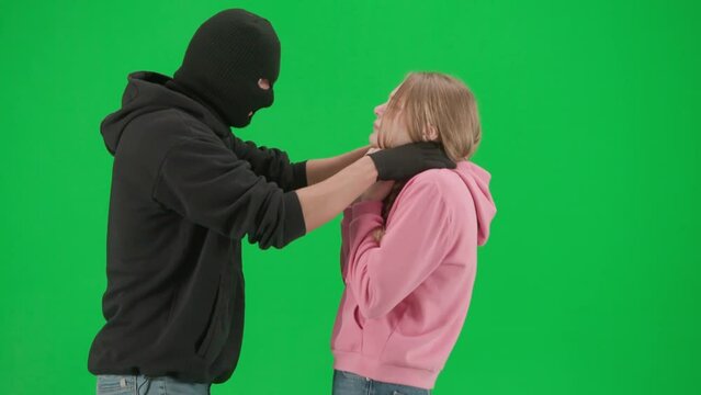 Portrait of thief and victim on chroma key green screen background. Girl stepping back, man robber walking threatening her, catches begins to strangle girl.