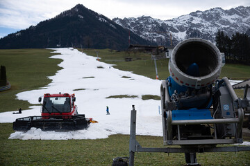 Snow groomer (snow cat, piste machine or trail groomer) and snow cannon are waiting to be used to prepare the ski trails in the ski area in Walchsee, Tyrol, Austria.  A ski lift (T-bar lift)