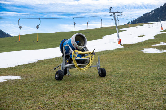 A snow cannon waiting to be used to prepare the ski trails in the ski area in Walchsee, Tyrol, Austria.  A ski piste and a ski lift (T-bar lift) in the background.