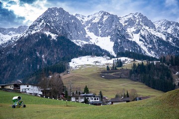 Zahmer Kaiser. View of mountain range in winter in Walchsee, Tyrol, Austria. Some houses and a snow cannon in the foreground in front of a green meadow - obrazy, fototapety, plakaty