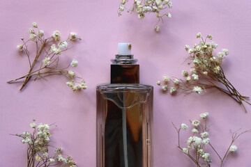 Unrecognizable perfume bottle and gypsophila flowers on pastel pink background. Flat lay.