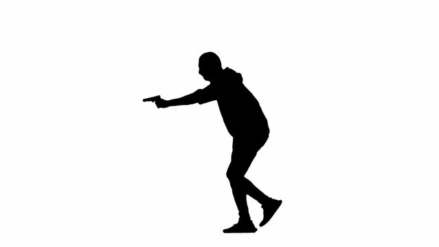 Black silhouette of thief on isolated white background. Male robber in hoodie and balaclava walking with a gun in his hands, preparing to commit a crime. Side view.
