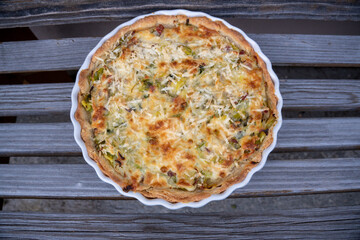 Quiche Lorraine in a tart pan fresh from the oven on a wooden bench
