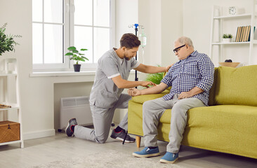 Male caregiver setting up iv drip to senior patient. Senior man sitting on sofa receiving intravenous treatment or vitamin therapy at home. Elderly healthcare, medical care, support