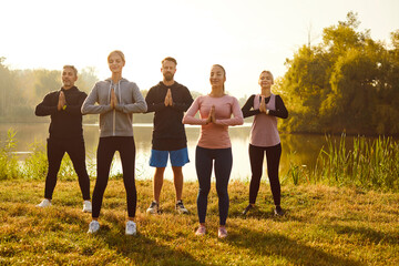 Group of fit and active people doing yoga exercises in nature. Happy smiling men and women in...