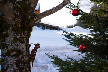 Artificial woodpecker on tree trunk and partial view of fir tree outdoors with a red Christmas tree...