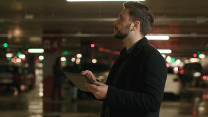 Caucasian adult man driver supervisor inspector investor businessman entrepreneur engineer inspecting underground parking check security measures with digital tablet use navigation on electronic pad