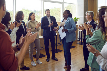Group of business people standing in a circle applauding their african americam woman colleague after meeting. Diverse company employees listening coworker with a report in conference room in office.