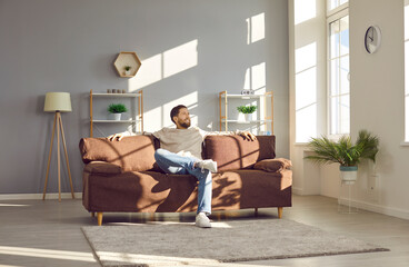 Relaxed man sitting on a comfortable couch at home. Happy young man enjoying free time and lounging...