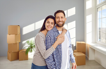 Portrait of a happy family couple in the new house on moving day. Young man and woman standing in a...