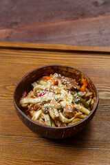 Wok udon noodles with beef and vegetables in a coconut shell plate
