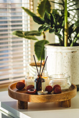 Aroma candles and reed diffuser with fruity sweet scent of tropics fruits. Litchi on a wooden tray, Bali oriental apartment interior concept. Modern room design, Scandinavian style. Relaxation at home