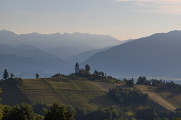 Church of Saint Primoz in Jamnik village, Slovenia, Europe. The church is on the ridge of the mountains. Sunrise, mountain peaks in the background.