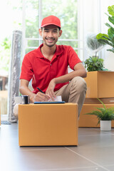 Portrait of young Asian man house moving service worker in uniform doing home relocation, checking list cardboard boxes for preparing to move. Smiling and looking at camera