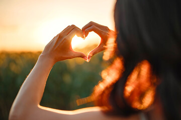 Young woman making heart shape with her hands at sunset, Love sign. - Powered by Adobe