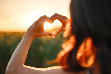 Fotobehang Young woman making heart shape with her hands at sunset, Love sign. © oatawa